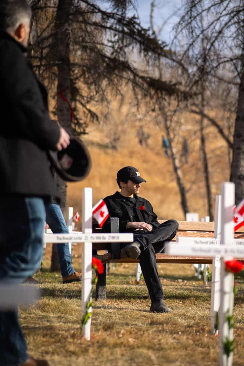 Man sits on bench in cemetery with canadian flags.